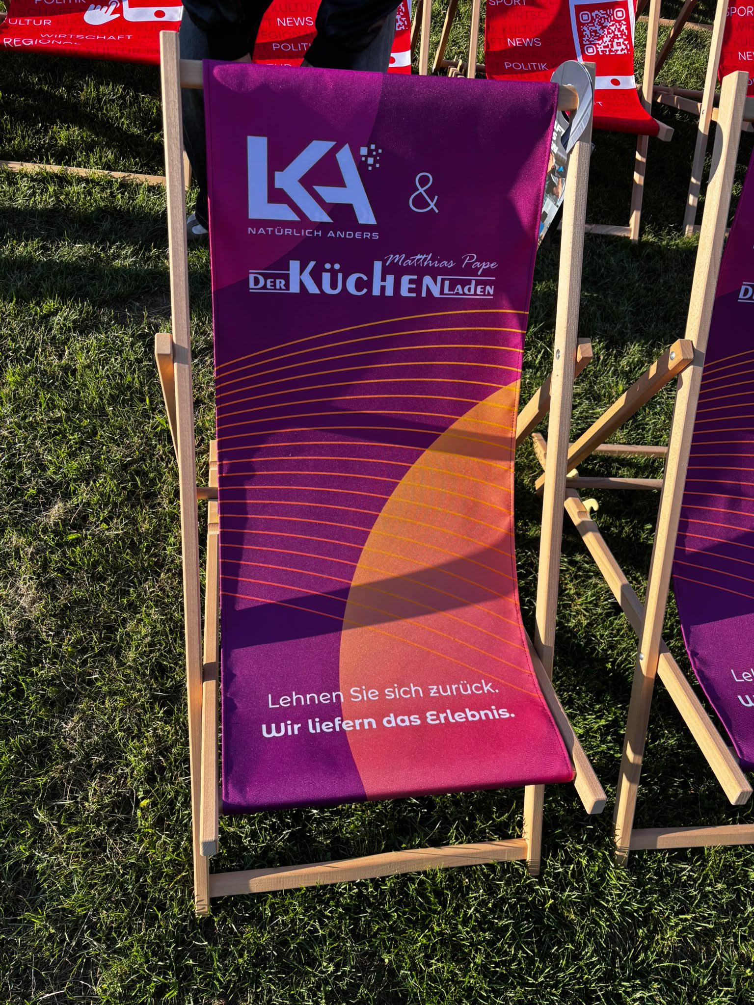 Lila Sonnenstuhl aus Holz mit Branding der LKA - Agentur und des Küchenladens Pape auf einer Wiese